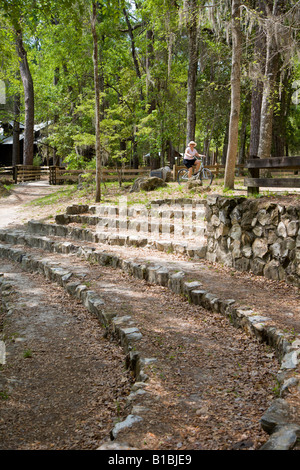 Ältere Frau fährt mit dem Fahrrad an Steinstufen des Amphitheaters im O'leno State Park in Florida vorbei Stockfoto