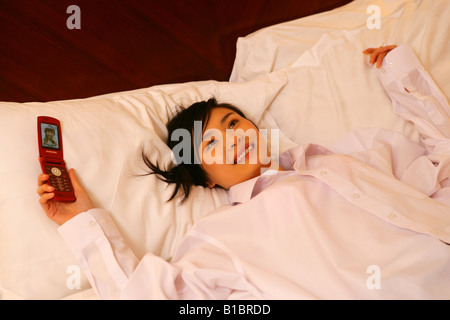 junge Frau auf Hotelbett liegend mit Handy Stockfoto