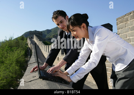 Kaukasische Geschäftsmann und chinesische Unternehmerin mit Laptop auf Mauer, Peking, China Stockfoto