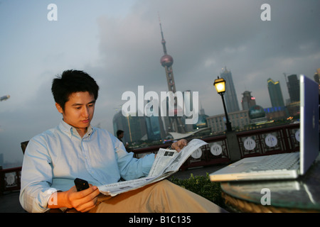 ein junger Mann liest Zeitung neben einem Tisch auf den Bund, Shanghai, China Stockfoto