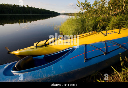 Blaue und gelbe Kajaks. Zwei aus Fiberglas oder Kunststoff Kajaks hochgezogen auf einem grasbewachsenen Ufer eine lange spiegelglatten See Stockfoto