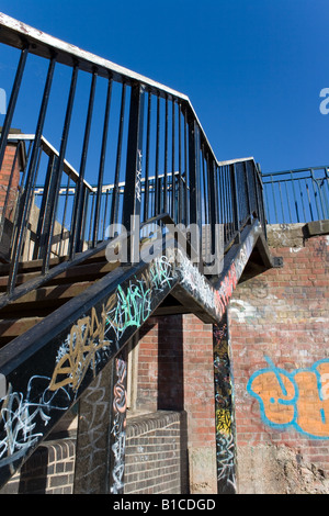 Handlauf aus Holz auf Metall Treppe mit flockige Farbe zum Kanal führt. Brücke-Wand auf der Rückseite geschliffen mit Graffiti auf sie kastriert. Stockfoto