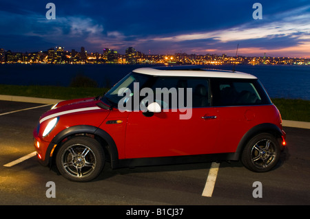 Ein Mini Cooper, mit Lichtern, genommen in der Abenddämmerung im Hintergrund eine beleuchtete Stadtbild. Stockfoto