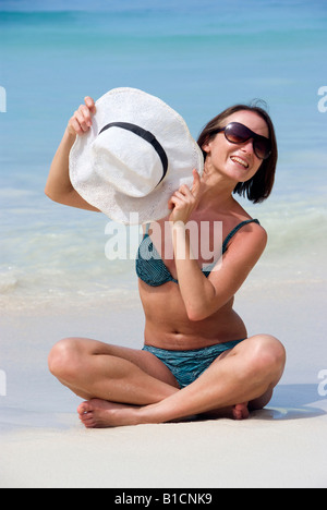 junge Frau im Bikini und mit Sonnenbrille am Strand, mit Hut Stockfoto