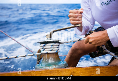 Ein Besatzungsmitglied an Bord Segeln Jolle Kurbeln SY Galatea auf einer Winde während der 2008 Antigua Classic Yacht Regatta. Stockfoto