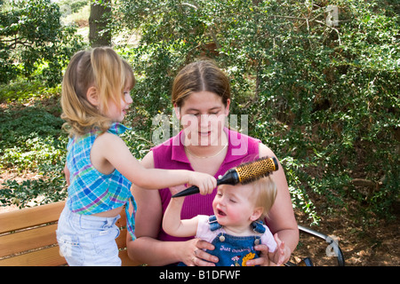 Mutter und ihre zwei jungen Töchter sprechen und spielen auf einer Holzbank in einem Park Modell veröffentlicht Stockfoto