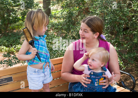 Mutter und ihre zwei jungen Töchter sprechen und spielen auf einer Holzbank in einem Park Modell veröffentlicht Stockfoto