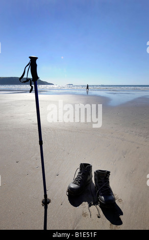 EIN EINSAMER WANDERER NIMMT EINE AUSZEIT VON IHREM SPAZIERGANG UND PADDEL IN DAS MEER AN DER WALISISCHEN KÜSTE, UK. Stockfoto