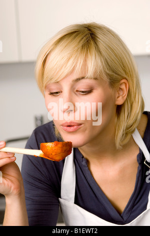 Nahaufnahme einer jungen Frau, die bläst Tomatensauce auf einem Holzlöffel Stockfoto