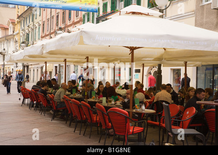 Gäste, die unter Sonnenschirmen im Café in der Fußgängerzone der Korzo Street im Stadtzentrum speisen und trinken. Rijeka Kroatien Stockfoto