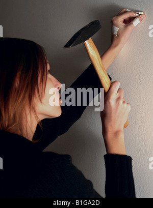 Eine Frau Nagel in die Wand Hämmern Stockfoto