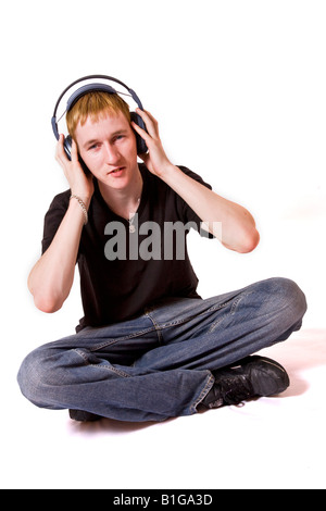 Ein junger Mann auf dem Boden sitzend hört Musik über Kopfhörer. Stockfoto