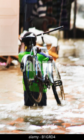 Afrikanischen jungen mit seinem Fahrrad getränkt in den Regen zu Fuß in die Gasse in Stonetown, Sansibar, Tansania, Afrika. Stockfoto