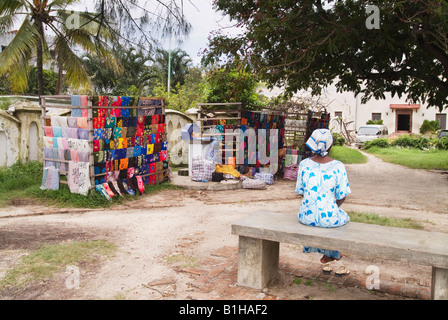 Afrikanische Frau, die in Stonetown Sansibar, Tansania, Ostafrika bei ihrem kleinen Outdoor-Laden mit traditionellen Khanga- und Kitenge-Stoffen sitzt. Stockfoto