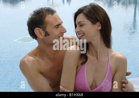 Ein paar sitzt dicht beieinander am Swimming pool Stockfoto