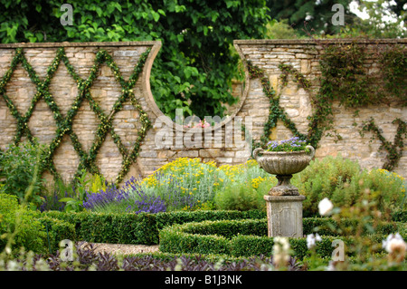 EINE ANTIKE STEINERNE URNE IN EINEM UMMAUERTEN GARTEN MIT ZWERG-BOX HEDGING UND EIN EFEU AUSGEBILDET IN EINEM GITTER DESIGN UK Stockfoto