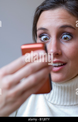 junge hübsche, Untertasse-eyed Frau liest eine SMS auf ihr Handy Stockfoto