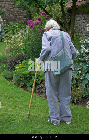 Ältere Frau mit Gehstock im Garten Stockfoto