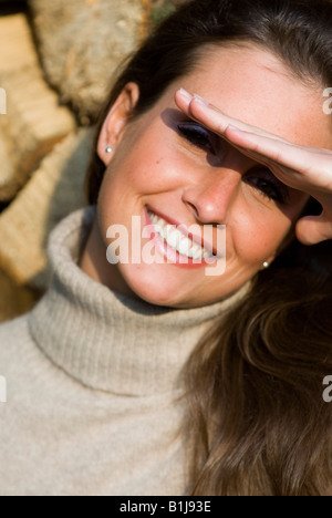junge Brownhaired Frau trägt einen Rollkragenpullover, hielt eine Hand über ihre Augen, lächelnd Stockfoto