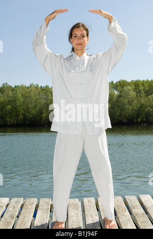 junge hübsche Frau praktizieren Tai Chi auf einem Holzsteg am See, bekommen das Qi Stockfoto