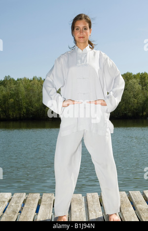 junge hübsche Frau praktizieren Tai Chi auf einem Holzsteg am See, bekommen das Qi Stockfoto