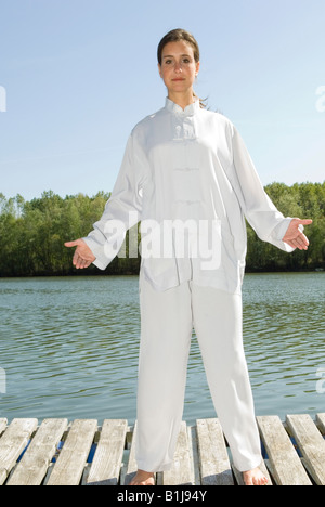 junge hübsche Frau praktizieren Tai Chi auf einem Holzsteg am See, bekommen das Qi Stockfoto