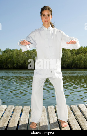 junge hübsche Frau praktizieren Tai Chi auf einem Holzsteg am See, Grundlagen Stockfoto