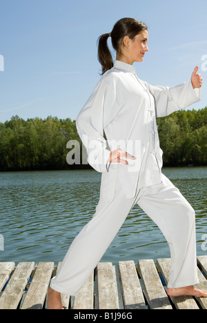 junge hübsche Frau praktizieren Tai Chi auf einem Holzsteg am See, Griff Vögel Heck Stockfoto