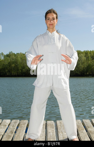 junge hübsche Frau praktizieren Tai Chi auf einem Holzsteg am See Stockfoto