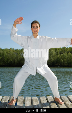 junge hübsche Frau praktizieren Tai Chi auf einem Holzsteg am See Stockfoto