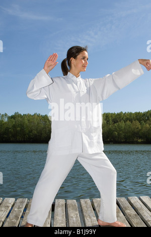 junge hübsche Frau praktizieren Tai Chi auf einem Holzsteg an einem See, Übung, Handhaltung Stockfoto