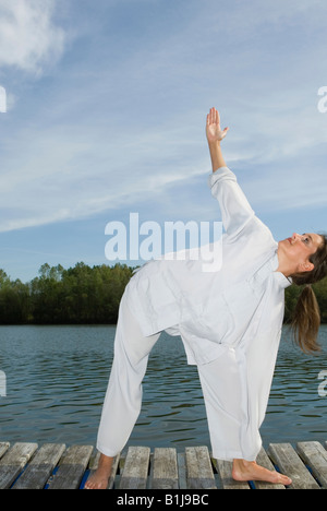 junge hübsche Frau auf einem Holzsteg am See, Trikonasana-Dreieck, Yoga zu praktizieren Stockfoto