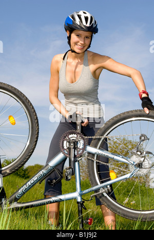 junge Frau mit Helm, Reparatur ihr Mountainbike auf einer Wiese Stockfoto