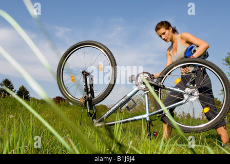 junge Frau mit Helm, Reparatur ihr Mountainbike auf einer Wiese Stockfoto