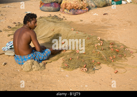 Ein Mann heilt seine Fischernetze am Strand von Thangasseri in der Nähe von Kollam in Kerala, Indien. Stockfoto