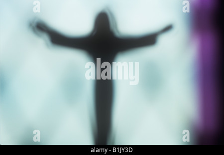 Impressionistische Jesus Christus-Figur mit ausgestreckten Armen Silhouette gegen lila umrandete Fenster Stockfoto