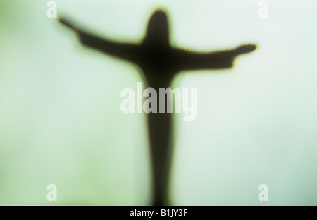 Impressionistische Jesus Christus-Figur mit ausgestreckten Armen Silhouette gegen blass grün-weißen Fenster Stockfoto