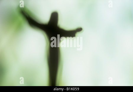 Impressionistische Jesus Christus-Figur mit ausgestreckten Armen Silhouette gegen blass grün-weißen Fenster Stockfoto