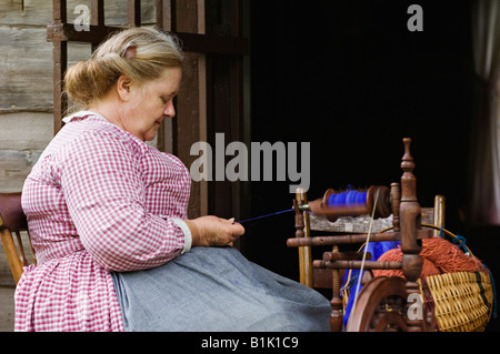 Ältere Frau in historischen Kostümen auf Veranda Kabine Spinnen Wolle in Pioneer Village im Frühjahr Mill State Park Stockfoto