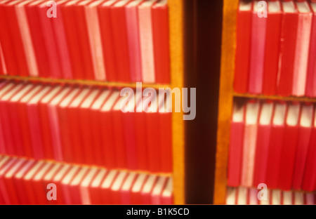 Impressionistische Reihen von nahezu identische roter Text oder Hymne oder Gebetsbücher in zwei Bücherregale in warmes Licht Stockfoto