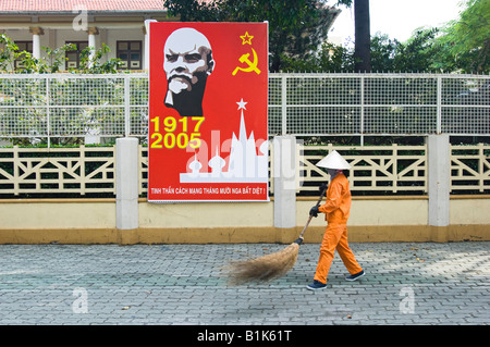 Frau fegt die Straßen neben kommunistische Propaganda-Plakat in Ho-Chi-Minh-Stadt, Vietnam. Stockfoto