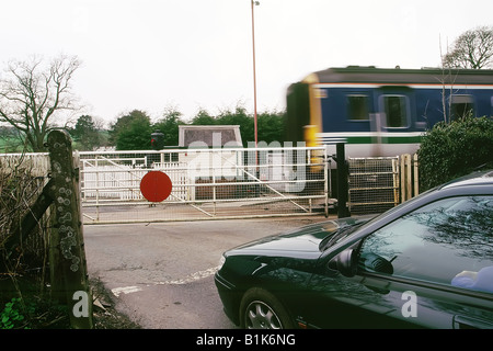 Ein Auto wartet auf eine bemannte Bahnübergang, als ein Zug vorbei, in Cumbria Geschwindigkeiten Stockfoto