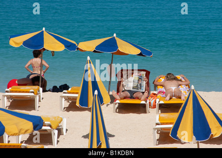 Mann liest Zeitung, während seine Partnerin sonnt sich. Playa de Los Amadores in der Nähe von Puerto Rico auf Gran Canaria. Stockfoto