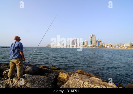 Ein Mann, Angeln in der Nähe von Tel Aviv Beach mit glitzernden Wolkenkratzer-Skyline der Stadt im Hintergrund. Foto in Tel Aviv, Israel Stockfoto