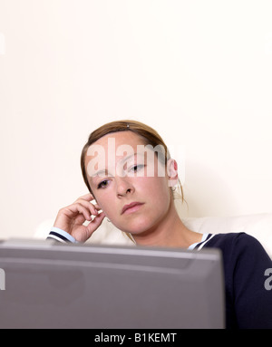 Nachdenkliche junge Frau, die mit Blick auf Computer Geröll, während Gesicht streicheln Stockfoto