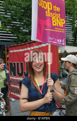 Junge Frau grinst wie sie "Stop die faschistischen BNP" Plakat vor NUJ Banner an Liebe Musik hasse Rassismus März hält Stockfoto