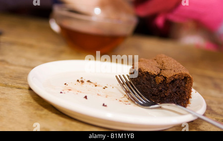 Stück frischer Schokoladenkuchen auf einen Teller mit einer Gabel und einer Tasse Tee im Hintergrund Stockfoto