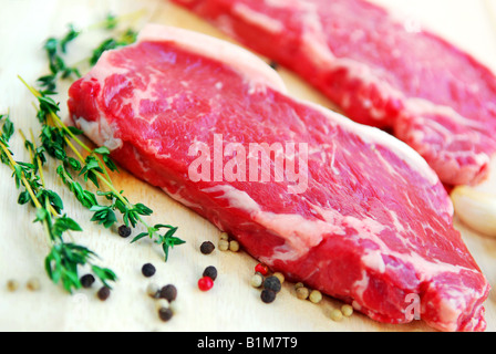 Zwei rohe New York Steaks auf Schneidebrett mit Thymian und Pfefferkörner Stockfoto