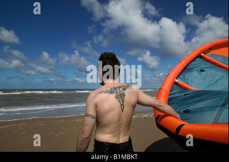 Kitesurfer mit einer Tätowierung auf dem Rücken festhalten an seinem Kite und Blick auf den Horizont am Strand von North Wales UK Stockfoto