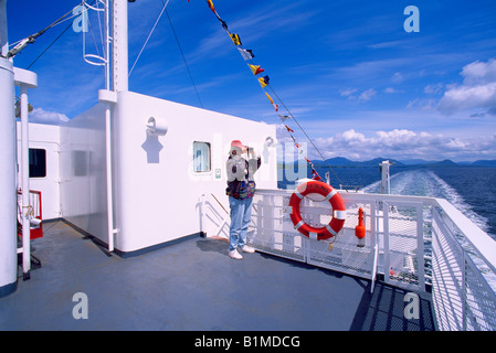 Frau, die durch ein Fernglas auf BC Fähre Segeln in Klemtu Kanal, BC, Britisch-Kolumbien, Kanada - Discovery Coast Stockfoto